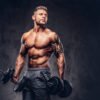 Handsome shirtless tattooed bodybuilder wearing sports shorts, posing in a studio.